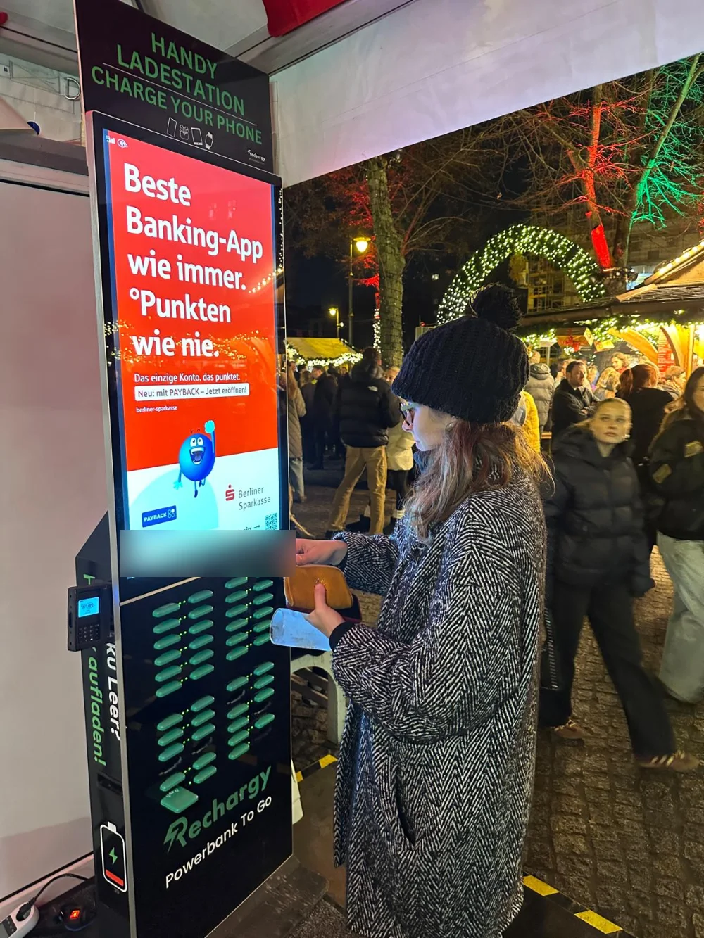 Besucherin an einer Berliner Sparkasse gebrandeten Rechargy Station auf dem Weihnachtsmarkt